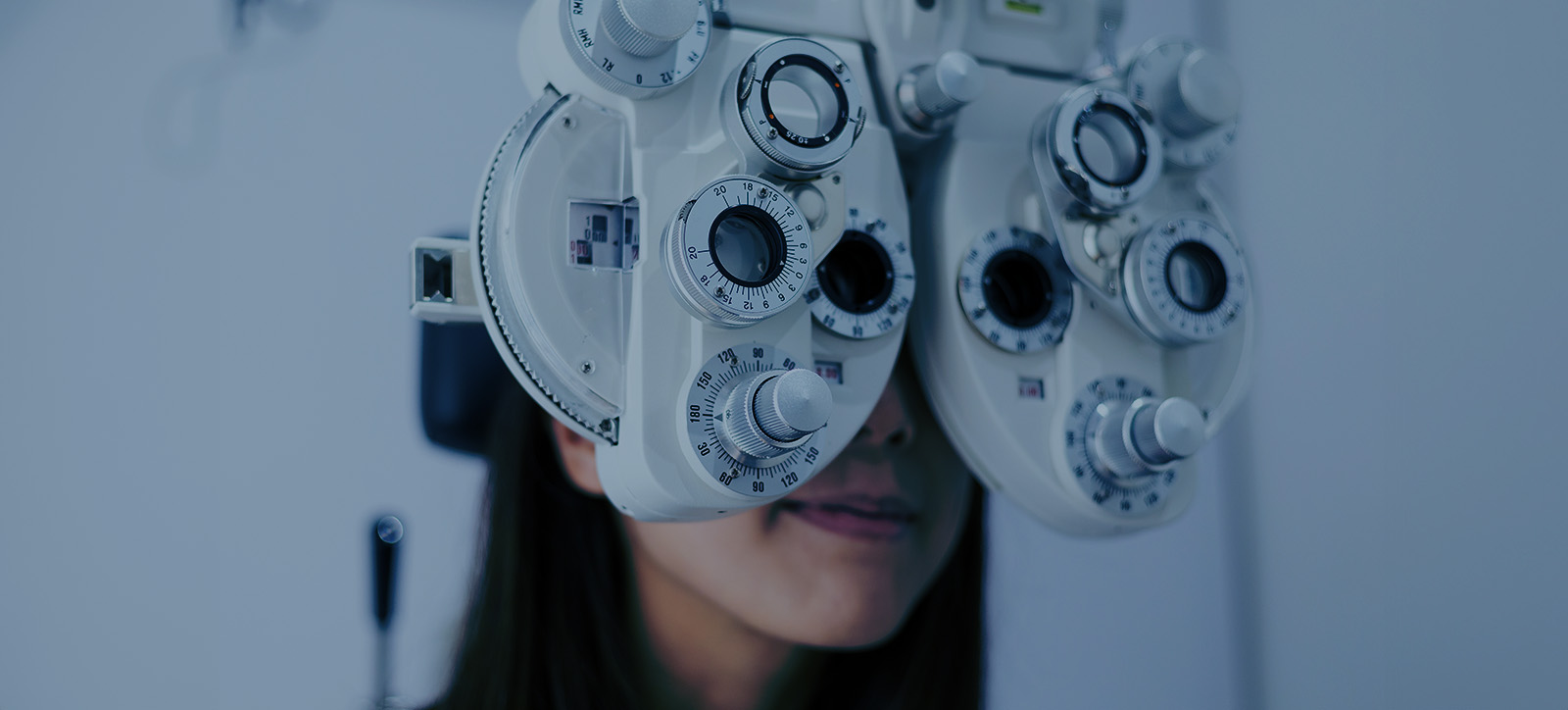A woman wearing glasses over her eyes while sitting at an eye exam machine.
