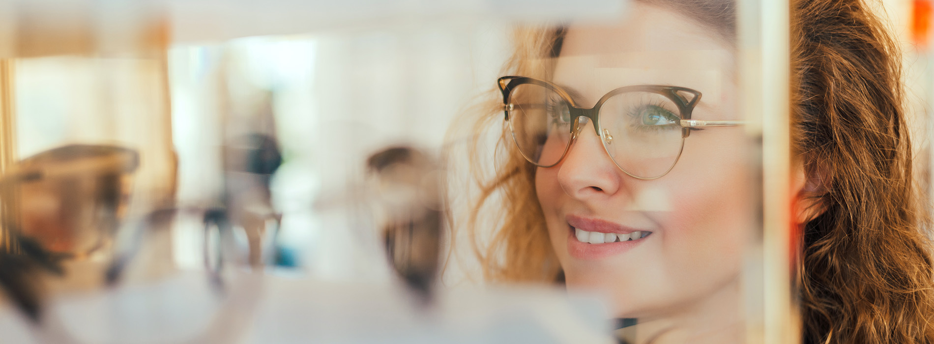The image shows a woman with glasses smiling at the camera, set against a blurred background featuring indistinct people and objects, possibly taken from a smartphone screen displaying a photo collage app.