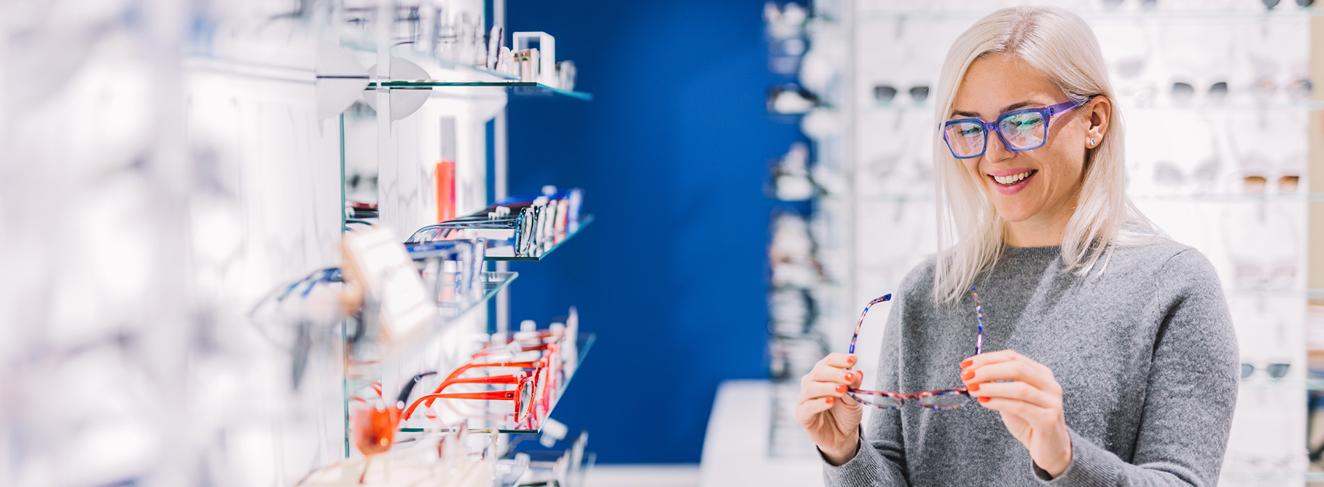 A woman with glasses stands behind a display case filled with various items, likely at an eyewear store.