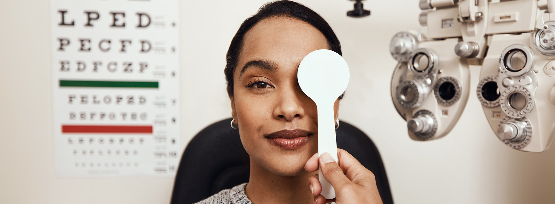 A woman holding a magnifying glass over her eye while seated at an optometrist s chair.