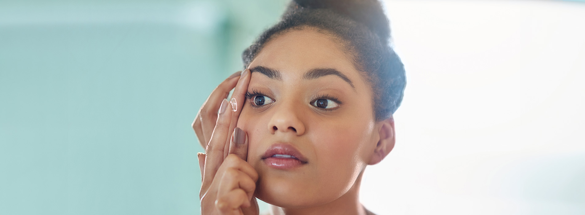 A woman applying makeup on her face, captured in a close-up view.