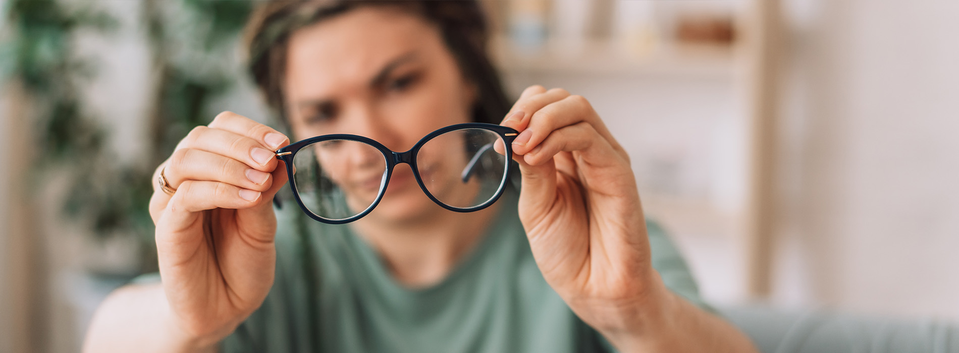 A woman holding a pair of glasses up to her eyes with a focused expression.
