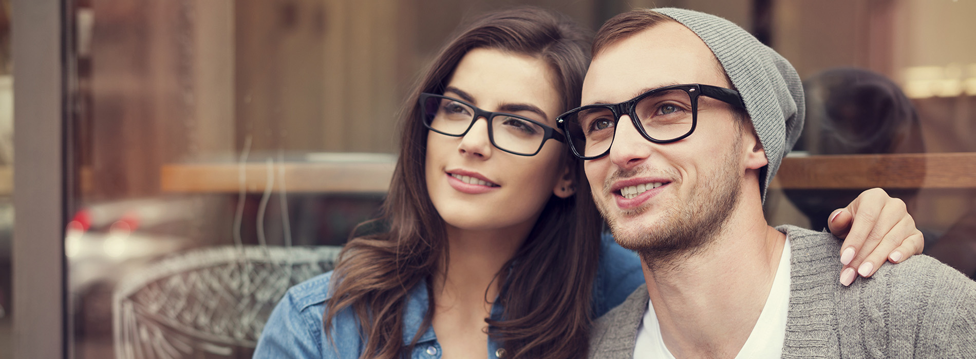 A young couple posing together with a warm smile, the man wearing glasses, both holding onto each other.