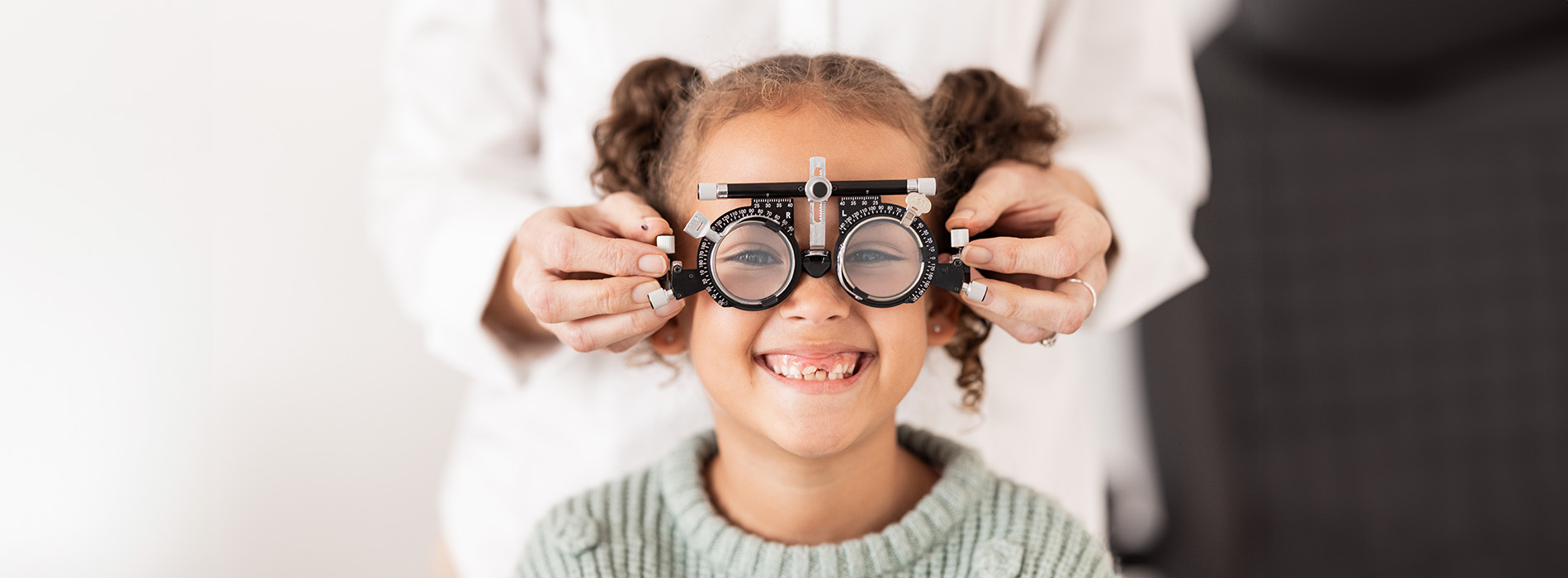 A young girl being fitted with glasses by an adult, likely in an optician s office setting.