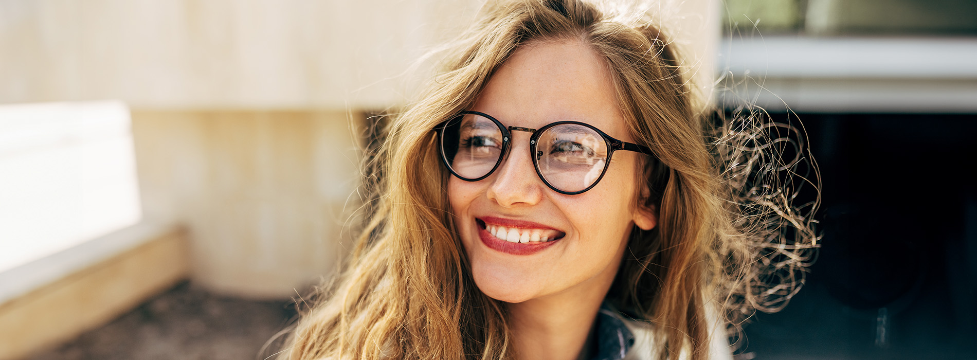 The image shows a person with glasses smiling at the camera against a blurred background.