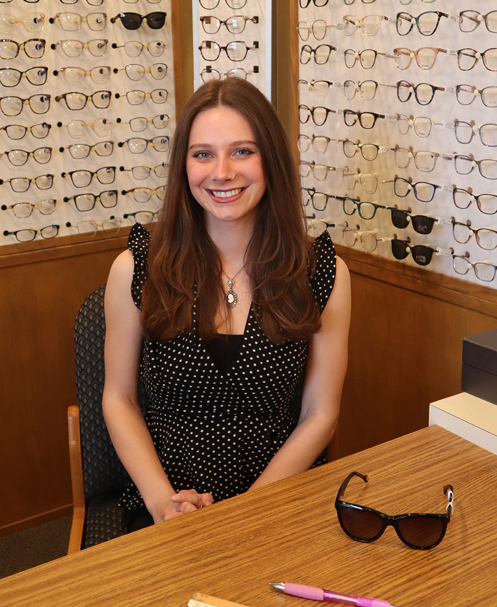 A young woman with glasses sitting at an optical store counter.