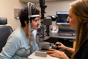 A woman with glasses is assisting an elderly person during an eye exam at an optometrist s office.