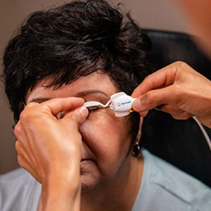 The image shows a person having their eyes checked with an eye exam device, likely at an optician s office.