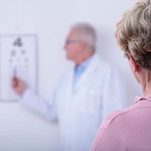 The image shows a man standing behind a display board with various diagrams, likely related to vision or medical procedures, while a woman reads from a chart on the board.