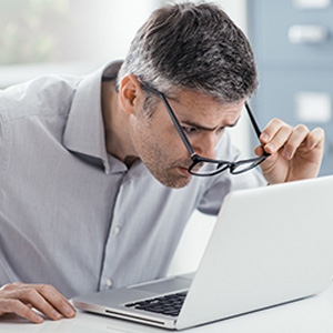 A man wearing glasses is looking intently at his laptop computer with his hands on the keyboard.