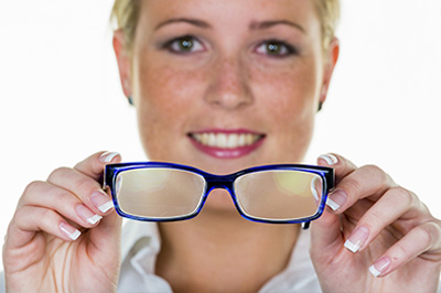 The image shows a woman wearing glasses, holding them up to her eyes with both hands, smiling at the camera.