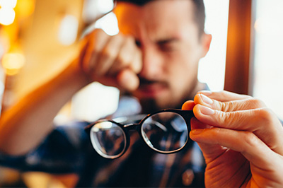 A man holding glasses in his hand, looking down with an expression of concern or contemplation.