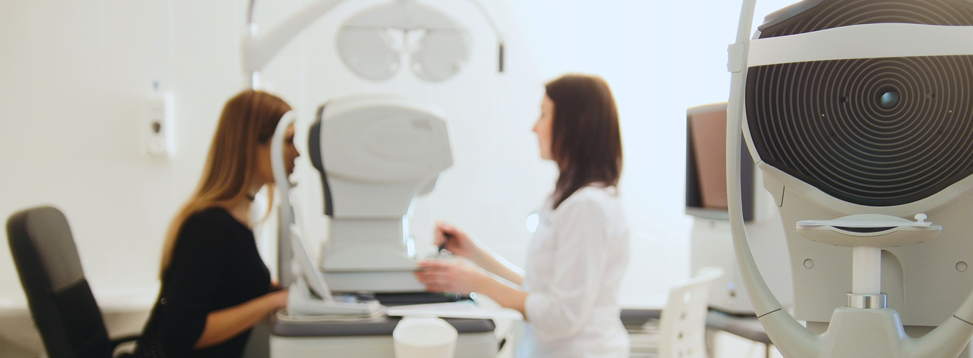 The image depicts an office setting with two individuals standing near a modern piece of equipment, possibly related to medical or dental services, and a woman seated at a desk with a computer monitor.