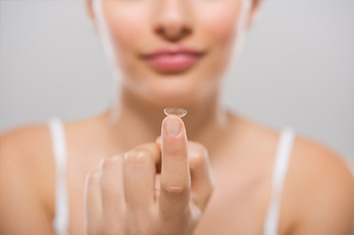 The image displays two photographs of a person s hand holding a small object, which appears to be a lens or a transparent disc, against their skin.