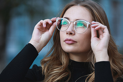 A woman wearing glasses with her eyes closed, looking upwards, against a blurred background.