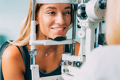 The image features a woman sitting in front of an eye exam machine, likely at an optician s office, with her eyes dilated for an examination.