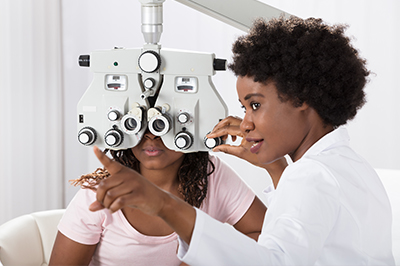 A woman wearing glasses with a large magnifying glass over her eyes while another person looks on, suggesting an eye examination in progress.