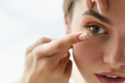 Woman applying makeup on her face using a magnifying mirror.