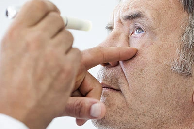 The image shows a person examining another individual s eye with a device, possibly a medical professional conducting an eye examination.